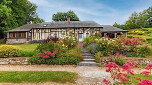 Una casa de estilo Tudor con base de piedra, techo de paja y un jardín con diversas flores y arbustos de colores.