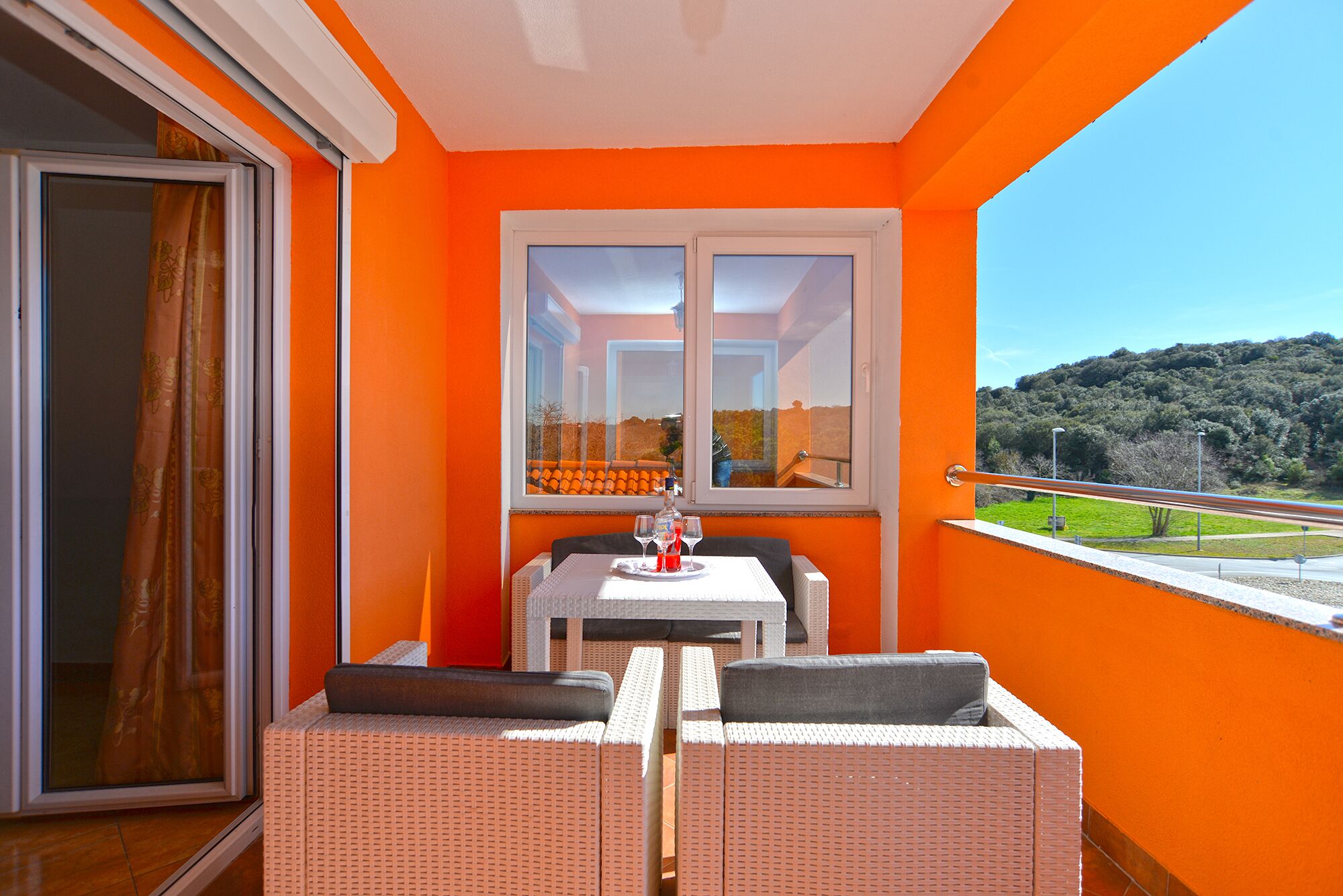 A balcony with orange walls, a table with two chairs, and a view of a green landscape.