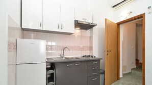 A compact kitchen with white cabinets, a built-in gas stove, a stainless steel sink, and a refrigerator.