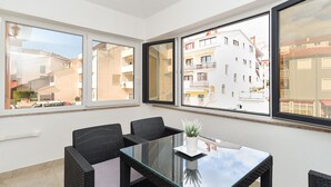 A balcony with a glass table and wicker chairs, overlooking a residential area with buildings and a clear sky.