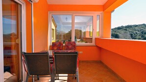 A balcony with two chairs, a table, and a view of a forested hill. - Apartment 2222/67254 (Istria - Pula), 500m from the beach (Pula)