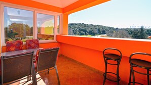 A balcony with orange walls, a table, two chairs, and a view of a forested area. - Apartment 2222/67254 (Istria - Pula), 500m from the beach (Pula)