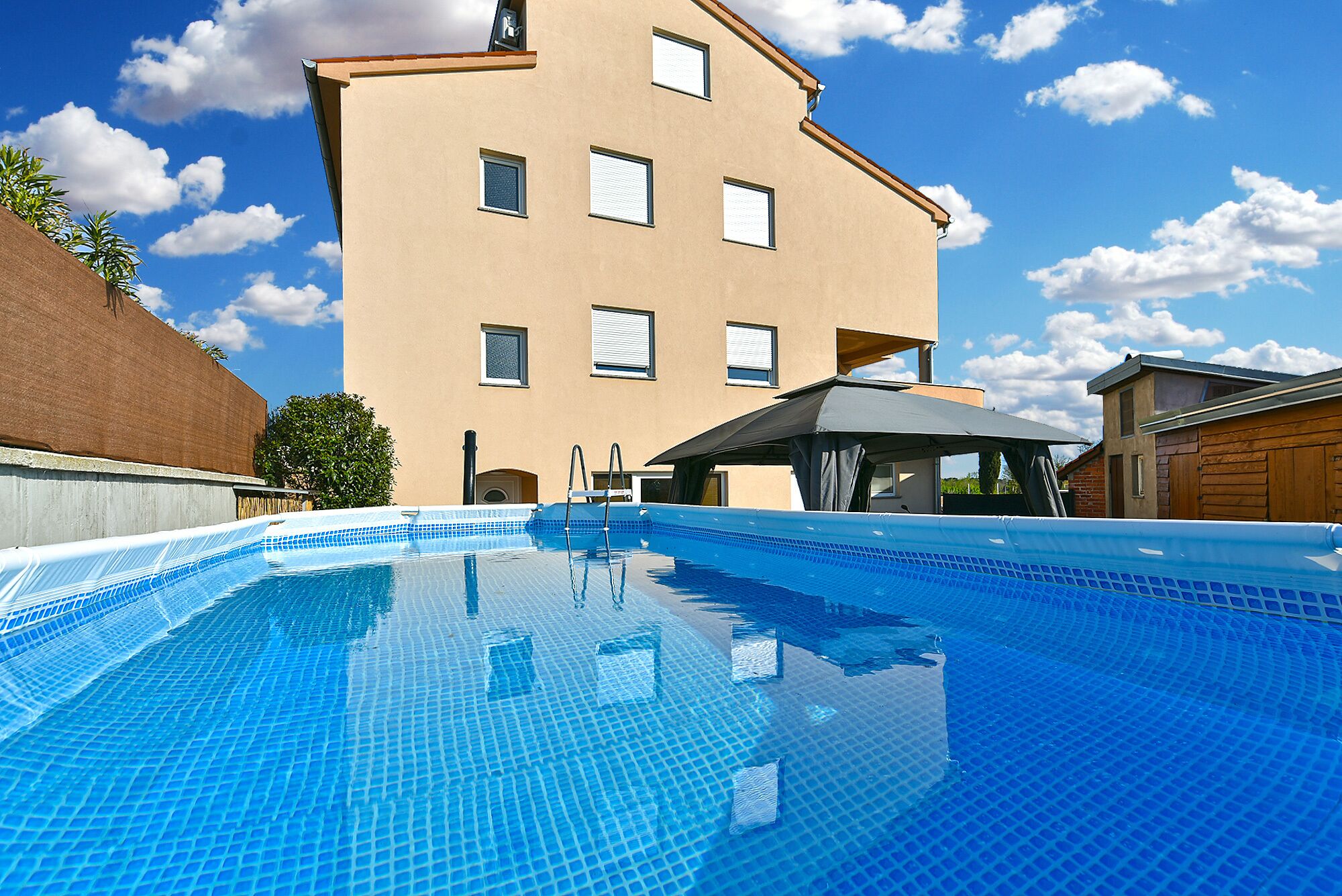 A swimming pool with a clear blue tiled surface, a building with multiple windows in the background, and a clear sky.