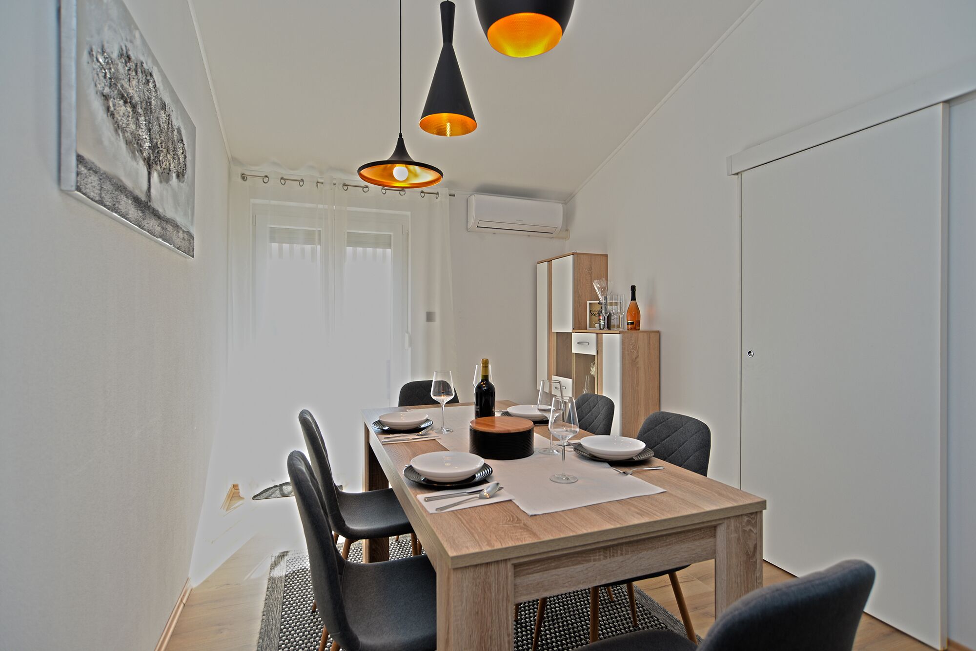 A dining area with a wooden table set for four, black chairs, and pendant lighting.