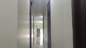 Um corredor comprido e estreito, com paredes brancas e chão de azulejos.