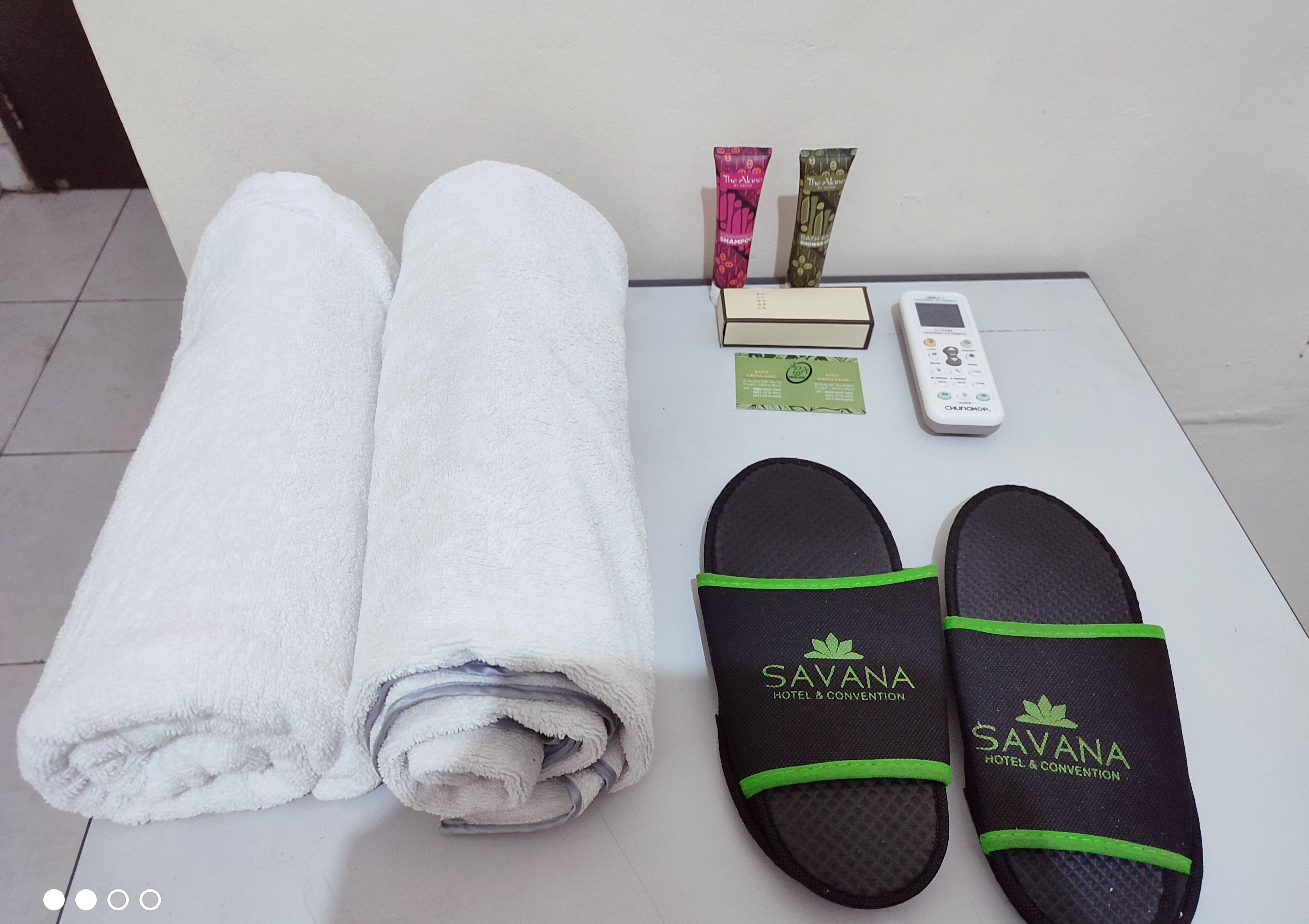 A neatly folded white towel, a pair of black slippers with green accents, a small white device, and two tubes of shampoo on a white surface.