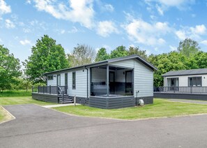 A single-story mobile home with a porch, large windows, and a grassy lawn.