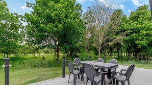 Un patio exterior con una mesa y sillas, rodeado de árboles y césped.
