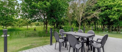 An outdoor patio with a table and chairs, surrounded by trees and a grassy area.