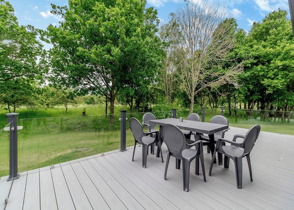 An outdoor patio with a table and chairs, surrounded by trees and a grassy area. - Coggeshall Lodge Pet (Earls Colne, Colchester)