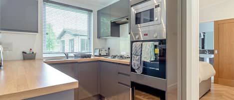 A modern kitchen with a built-in oven, microwave, and a window with blinds.
