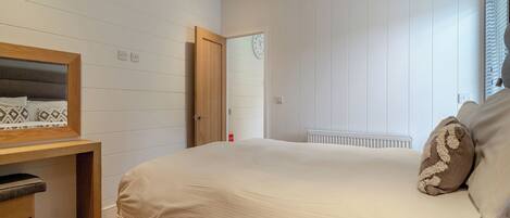 A bedroom with a bed, a bedside table, a mirror, and a window with blinds.