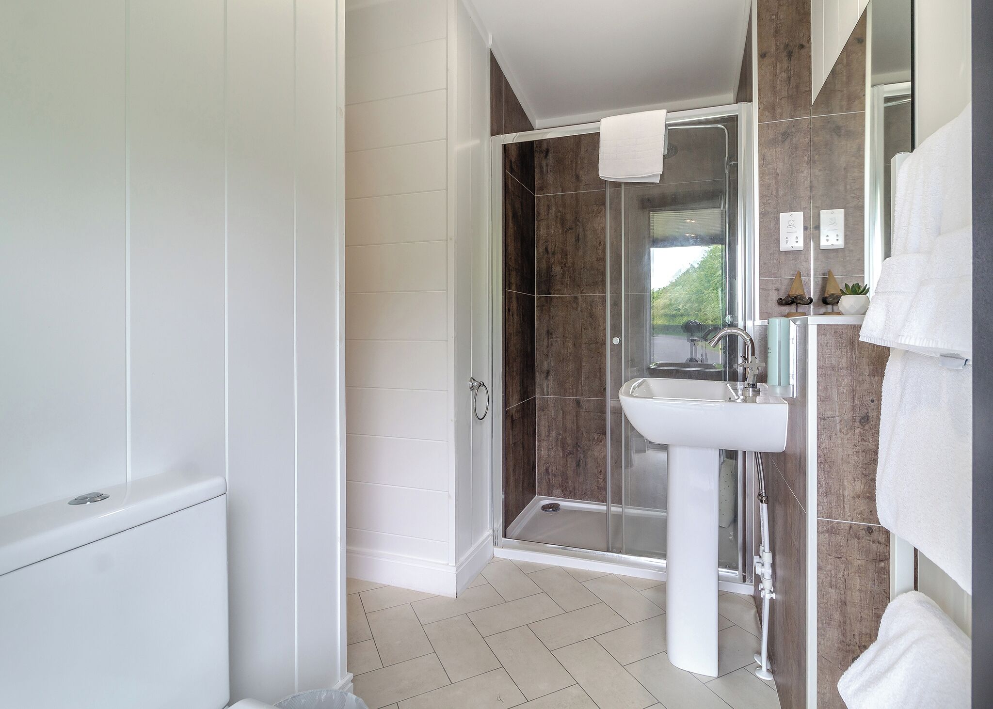 A modern bathroom with a glass shower enclosure, a white sink, and a mirror with a towel.