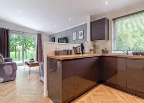 A modern kitchen with a wooden countertop, dark cabinets, and a large window with blinds.