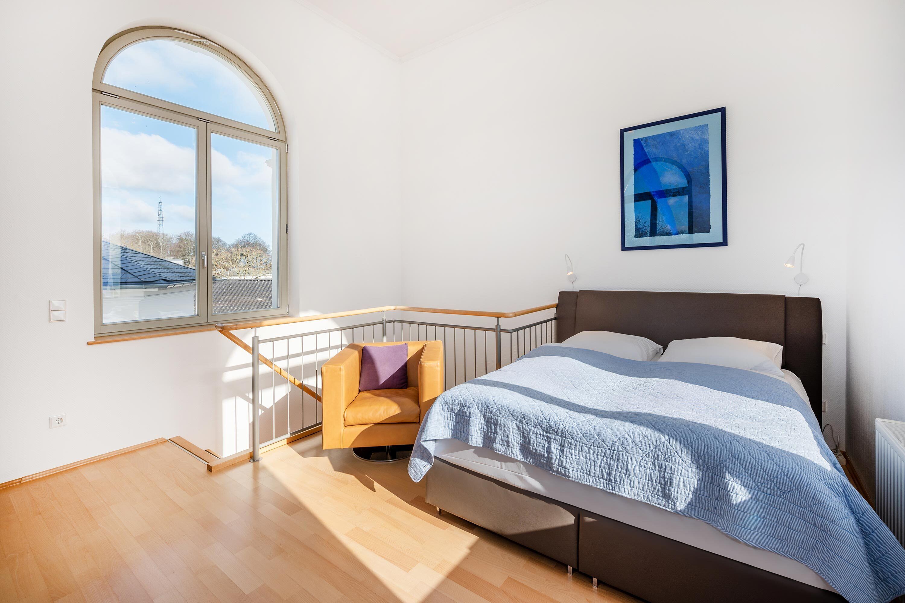 A bedroom with a large bed, a chair, a window, and a painting on the wall.