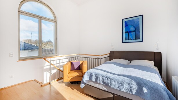 Ein Schlafzimmer mit einem großen Bett, einem Sessel, einem Fenster und einem Bild an der Wand.