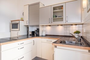 A modern kitchen with white cabinetry, a built-in oven, a coffee machine, and a sink with a faucet. - Vacation apartment in Heringsdorf with sea view, only 200 m from the beach (Seebad Heringsdorf)