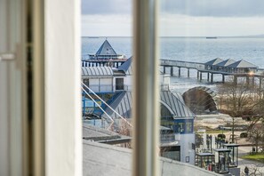 A coastal view with a pier extending into the water, a large building with a pointed roof, and a glass structure with signage.