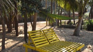 A yellow lounge chair under a palm tree on a sandy beach.