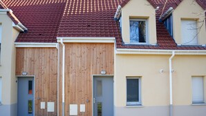 Ein zweistöckiges Gebäude mit rotem Ziegeldach, zwei Holztürfenstern und einer beige farbenen Fassade.