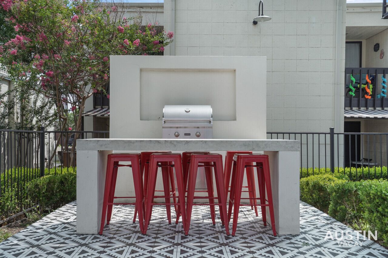 An outdoor bar area with a grill, four red stools, and a patterned floor.