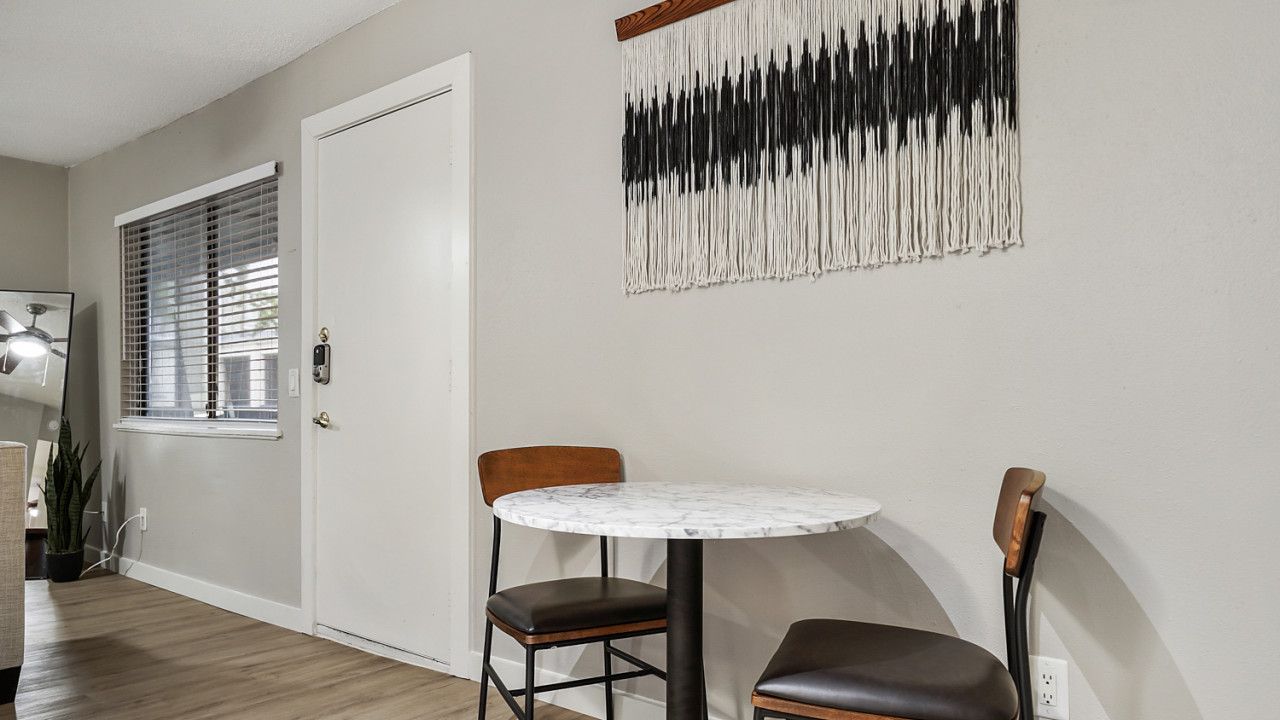 Un comedor con una mesa redonda y dos sillas, una puerta blanca y una obra de arte abstracta colgada en la pared.