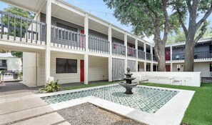 A multi-story building with balconies, a courtyard with a fountain, and a small garden area. - Amenity Heavy Serene Apt in Convenient Location (Austin)