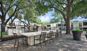 An outdoor seating area with a concrete table and metal chairs, surrounded by trees and a fence. - Amenity Heavy Serene Apt in Convenient Location (Austin)