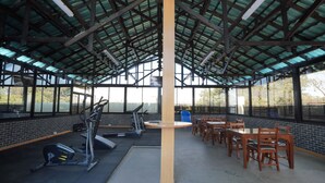 Un espacio cubierto para gimnasio con equipo de ejercicio, mesas y sillas.
