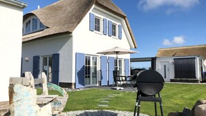 A house with a thatched roof, a patio with a grill, and a stone pathway leading to the house. - House in idyllic location with sauna, terrace and garden - Villa Morgensünn (Vaschwitz)