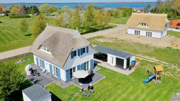 A large house with a thatched roof, a patio with outdoor furniture, and a play area with a slide. - House in idyllic location with sauna, terrace and garden - Villa Morgensünn (Vaschwitz)