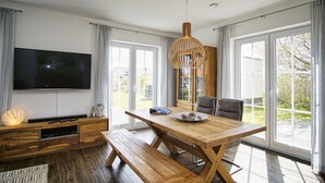 A modern living room with a wooden dining table, a large flat-screen TV, and a wooden bench. - House in idyllic location with sauna, terrace and garden - Villa Morgensünn (Vaschwitz)