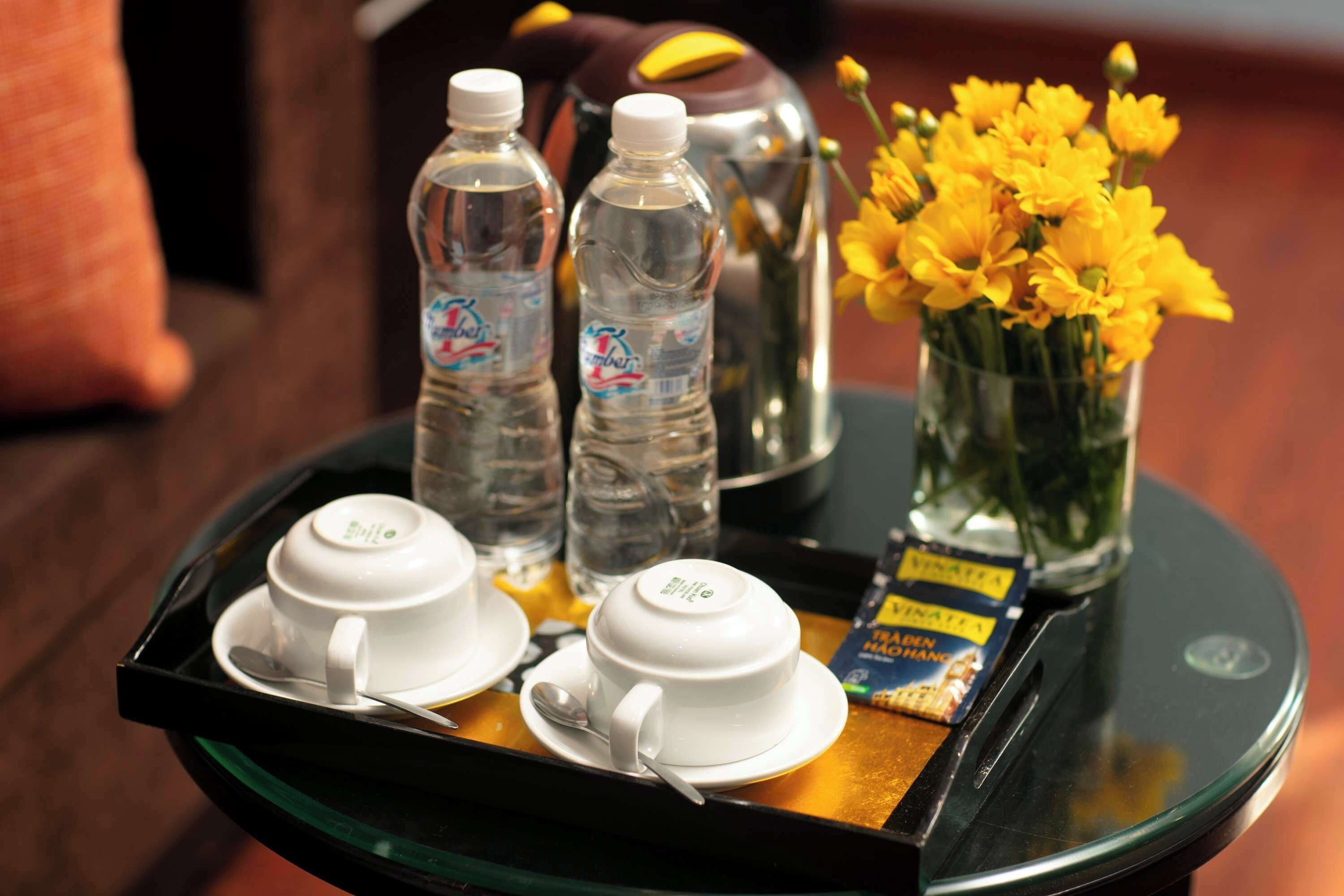 A tray with two white cups, two water bottles, a thermos, a vase with yellow flowers, and a box of snacks.