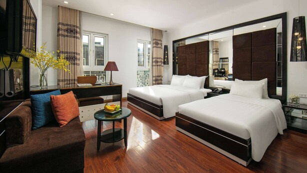 A modern hotel room with two beds, a sofa, a small table with fruit, and a large mirror. - THE SILK BOUTIQUE HOTEL & SPA (Hanoi)