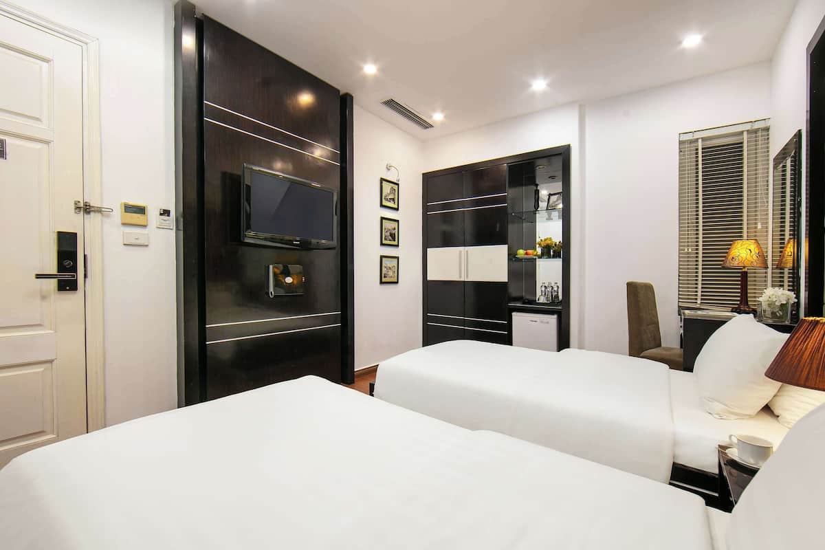 Quarto de hotel com duas camas, televisão, minibar e janela com persianas.