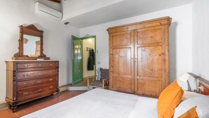 Et soveværelse med en trækommode, en stor garderobe, en seng med hvide sengetæppe og en stol.