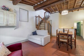 A living room with a white sofa, a red armchair, a wooden dining table with chairs, a staircase with wooden railings, and a chandelier. - Wine Apartments Florence Lambrusco (Firenze)