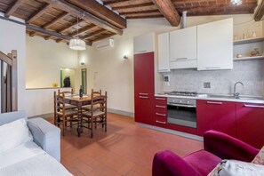 A compact kitchen with red cabinets, a dining area with a wooden table and chairs, and a modern pendant light. - Wine Apartments Florence Lambrusco (Firenze)