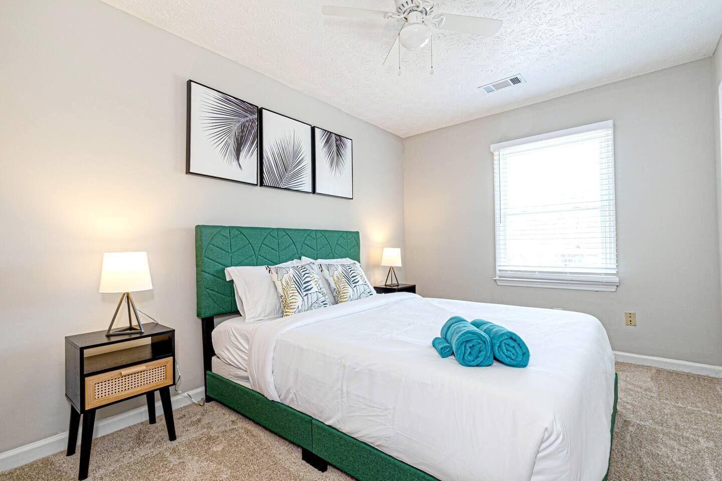 A neatly arranged bedroom with a bed, two bedside tables, a ceiling fan, and a window with blinds.