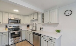 A modern kitchen with white cabinets, stainless steel appliances, a microwave, oven, dishwasher, and a clock on the wall.