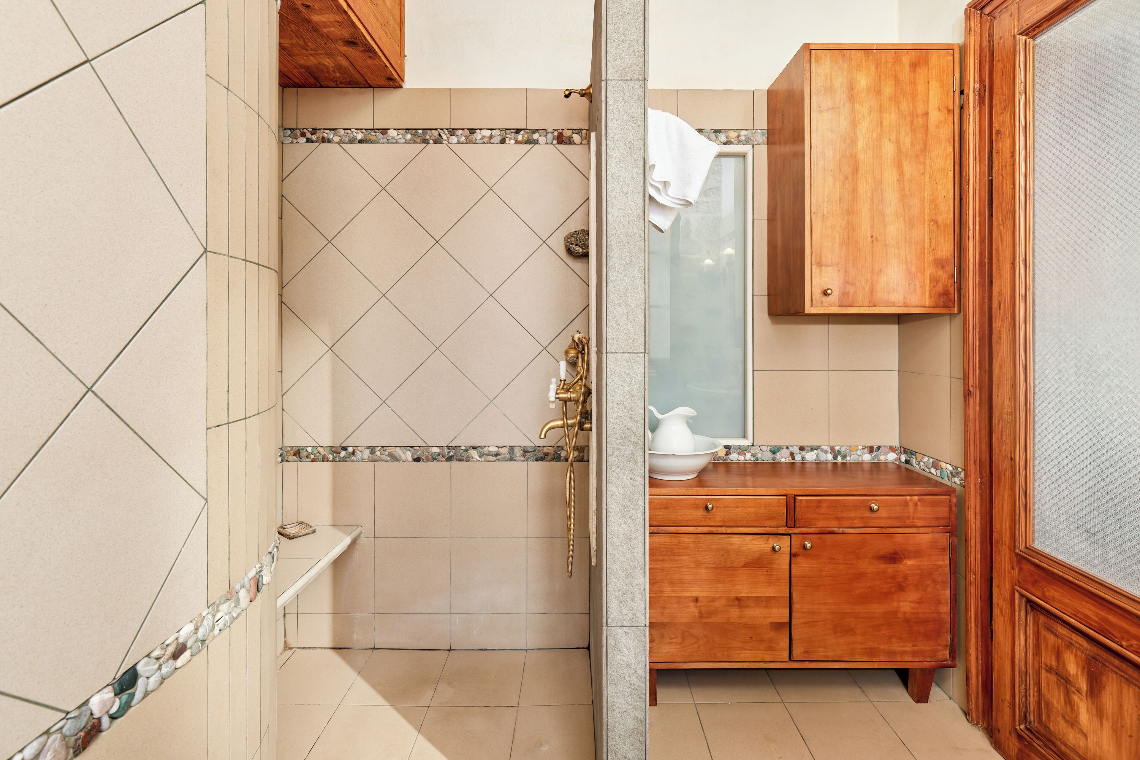 Een badkamer met een douche, een houten wastafelmeubel en een betegelde vloer.
