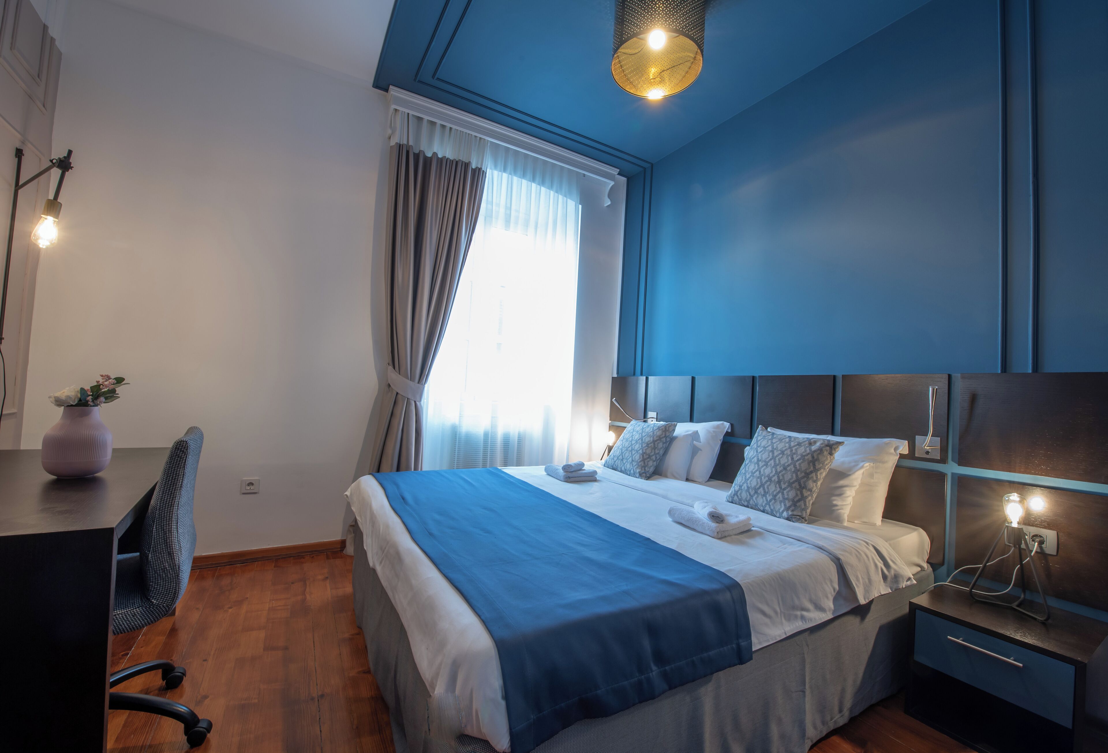 A modern bedroom with a large bed, bedside tables, a desk, and a chair.