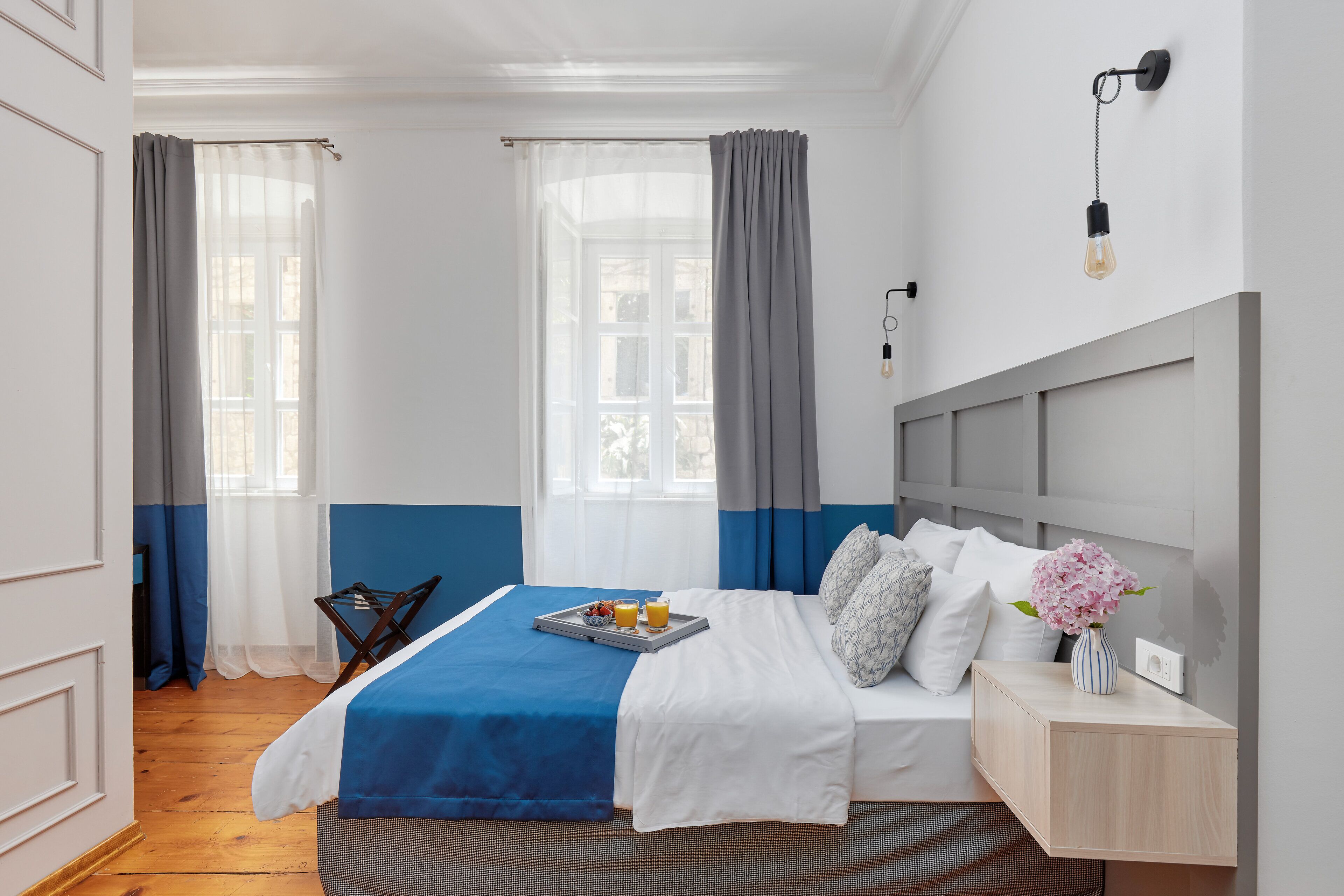 Een keurig opgemaakt slaapkamer met een bed, nachtkastje en een raam met gordijnen.