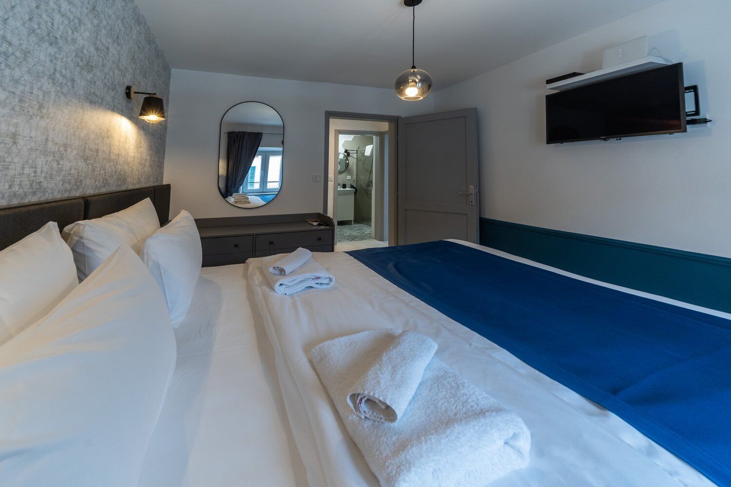 A hotel room with a bed, a desk, a mirror, and a TV.