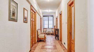 A hallway with wooden doors, framed pictures, and a seating area with chairs.