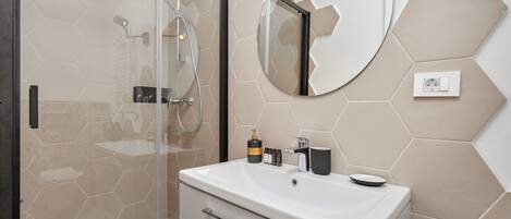 Un baño moderno con ducha envuelta en vidrio, un espejo redondo y un lavabo blanco con artículos de tocador.