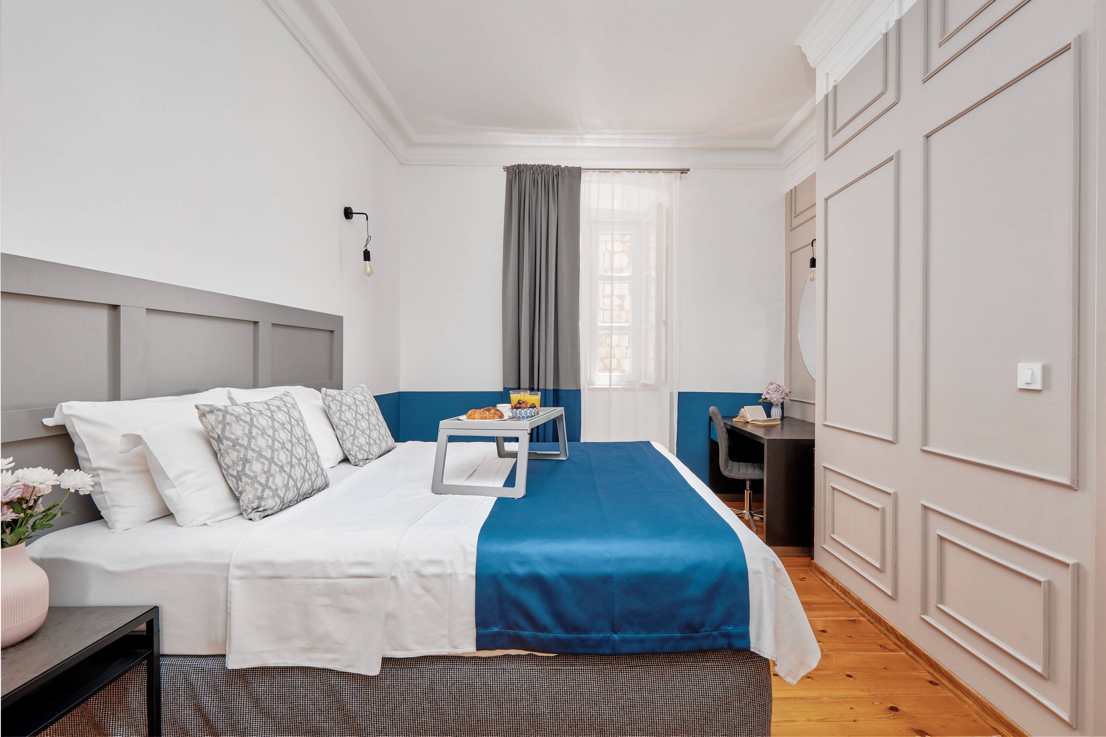 A neatly arranged bedroom with a bed, bedside table, and a small desk with a chair.