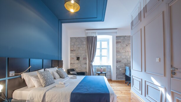 A modern bedroom with a large bed, a stone wall, and a window with curtains. - Kotor Nest (Kotor)