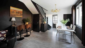 Ein modernes Wohnzimmer mit dunkler Farbgestaltung, einer Treppe, einem Essbereich mit Tisch und Stühlen sowie einem Kronleuchter.