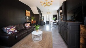 Ein modernes Wohnzimmer mit einer schwarzen Couch, einem runden Couchtisch und einem Essbereich mit Tisch und Stühlen.